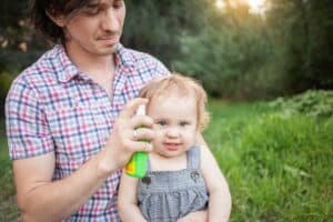 Dad treats his daughter with mosquito spray. The man uses spray on the child's arms and legs