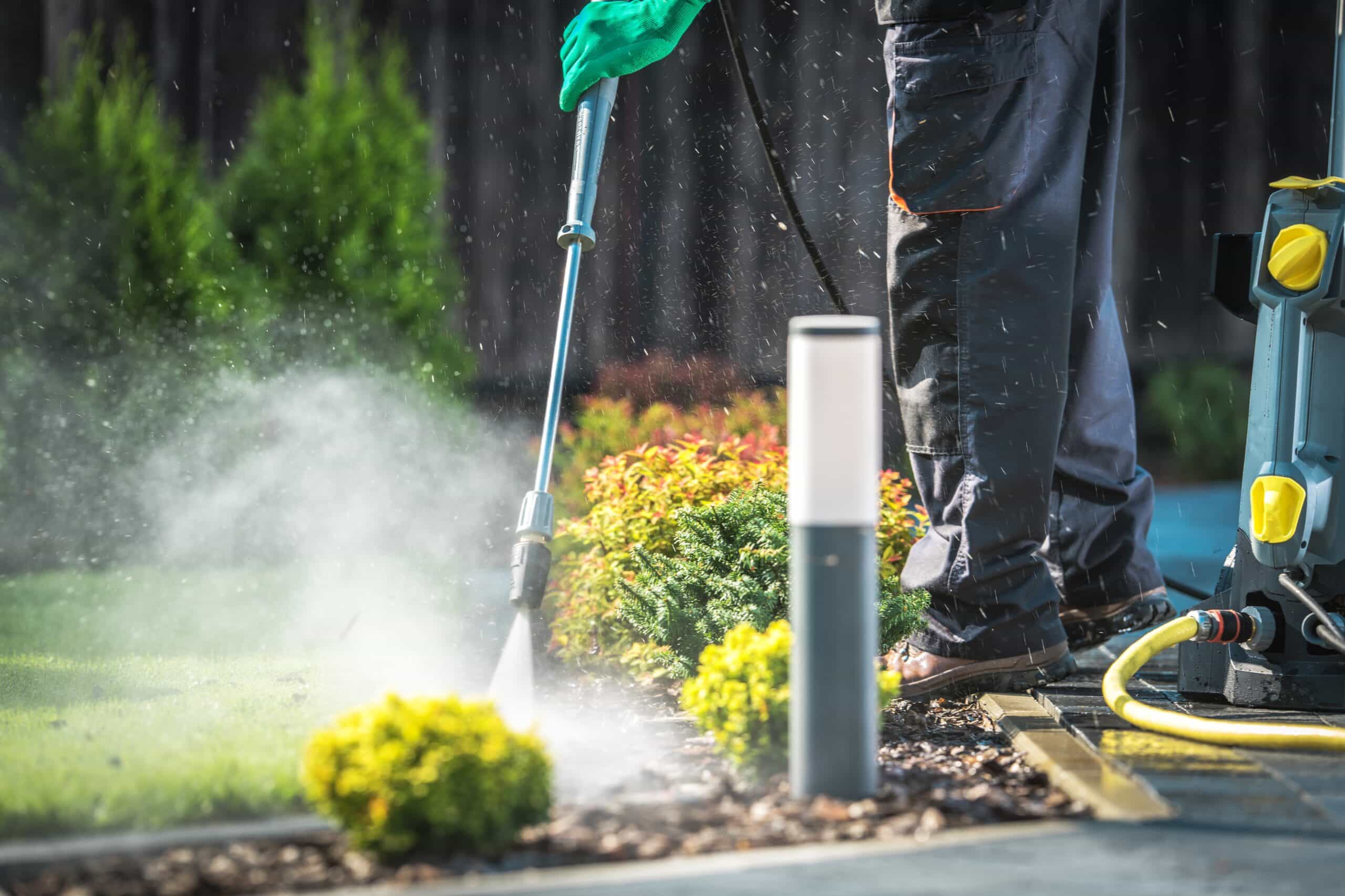 Technician applying a mosquito barrier along shaded shrubs beside a creekside fence in a Meadowbrook, Alabama backyard