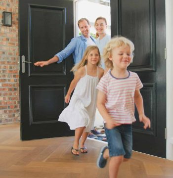 Family Returning Home With Excited Children Running Ahead Through Front Door